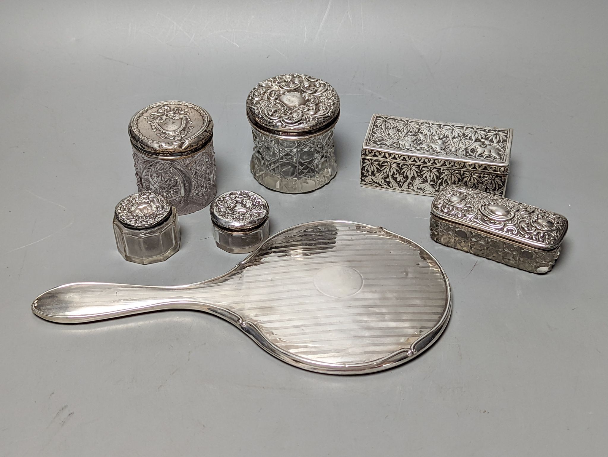 A silver mounted hand mirror, five assorted silver mounted glass toilet jars and an Indian white metal rectangular box.
